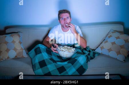 Lifestyle-Porträt von jungen attraktiven entspannten Mann beim Ansehen Film im Fernsehen Essen Popcorn sitzen spät in der Nacht im Wohnzimmer Sofa Couch genießen f Stockfoto