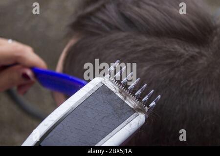 Detail des Haarschnitts vom Friseur. Der Friseur hält einen Kamm und einen elektrischen Rasierer in der Hand. Stockfoto