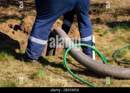 Mann Arbeiter, der Rohr hält und die Reinigung der Kanalisation im Freien bereitstellt. Die Abwasserpumpmaschine verstopft verstopfte Mannlöcher Stockfoto