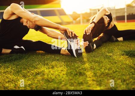 Athletischer Mann und Frau tun verschiedene Übung auf grünem Rasen Stockfoto