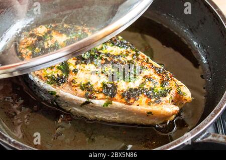 Gebratener roter Fisch in einer Pfanne unter dem Deckel. Lachs in Öl anbraten. Stockfoto