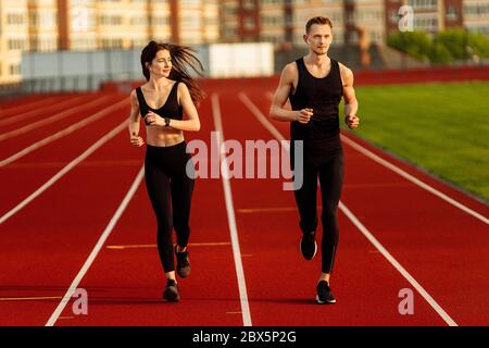 Junge Männer und Frauen laufen in schwarzen Sportanzügen im modernen Stadion. Stockfoto