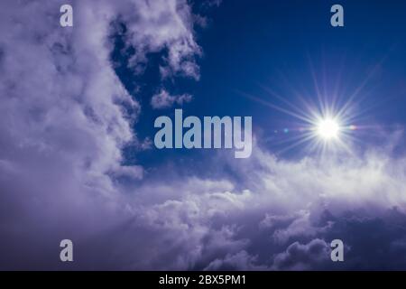 Natürliche Sonne scheint über Wolken in tiefblauem stürmischem Himmel Stockfoto