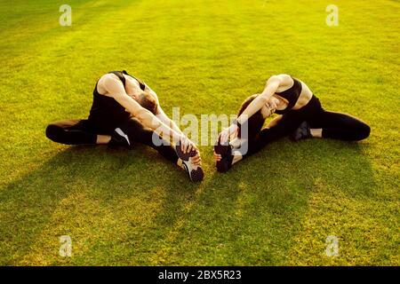 Junge sportliche Frau und Mann tun Stretching auf grünem Rasen. Stockfoto