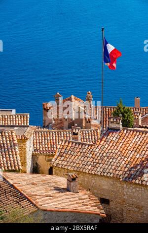 Terracotta Fliesen Dächer des Dorfes Eze mit französischer Flagge und das Mittelmeer. Französische Riviera, Alpes-Maritimes (06), Frankreich Stockfoto