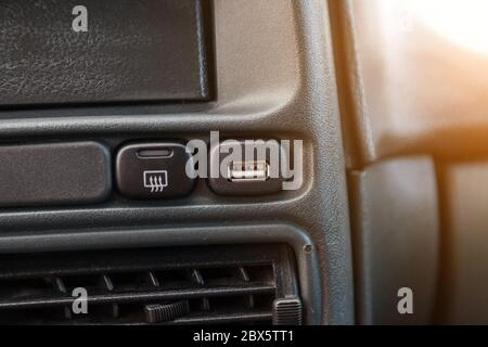 Nahaufnahme des usb-Eingangs zum Anschließen eines Ladegeräts oder Adapters für Geräte in der Nähe des Heizschalters der Heckscheibe auf einem schwarzen Bedienfeld aus Kunststoff. Stockfoto
