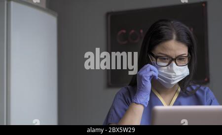Doktor arbeitet Computer in der medizinischen Praxis. Schöne asiatische Frau in Gläsern cprrects Maske beim Blick auf laptopa Bildschirm. Nahaufnahme Stockfoto