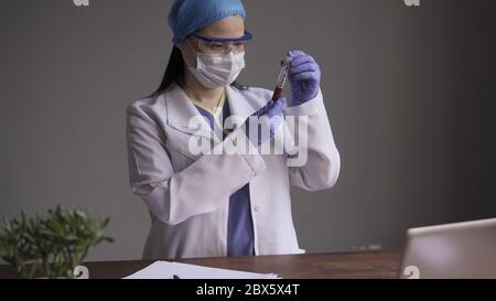 Laborassistent untersucht Reagenzglas mit Blut für Coronavirus-Test. Ärzteinferentin, die das Reagenzglas mit der Inschrift Covid 19 in sich hält Stockfoto