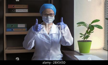 Positiver Arzt zeigt ermutigende Ja-Geste. Daumen hoch Geste von weiblichen medizinischen Worcer vor dem Hintergrund eines Krankenhauses Interieur Stockfoto
