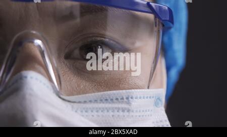 Schönes Auge eines müden Arztes, der eine Schutzbrille trägt. Asiatische Frau in Schutzbrille und Maske Blick auf Kamera. Nahaufnahme Stockfoto