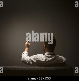 Geschäftsmann Schreiben mit Stift auf dunkelgrauen Wand. Blick von der Rückseite des Mannes in einem weißen Hemd macht Notizen, während auf der Couch sitzen. Leer oder Vorlage für Stockfoto