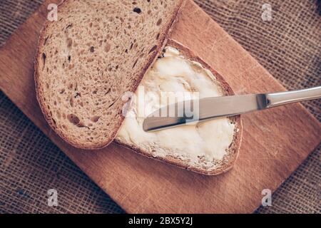 Nahaufnahme Scheibe Brot mit Butter und Messer auf dem Holztisch, Armutskonzept Stockfoto