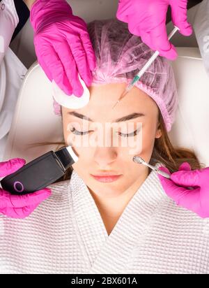 Nahaufnahme des schönen Gesichts einer jungen Frau. Viele Hände halten Kosmetologie Werkzeuge in der Nähe Gesicht eines Patienten Stockfoto