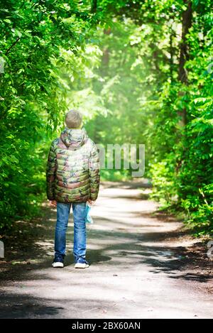 Junge Teenager trägt in Jacke mit Gesichtsmaske in der Hand ist rund um Park allein zu Fuß. Stockfoto