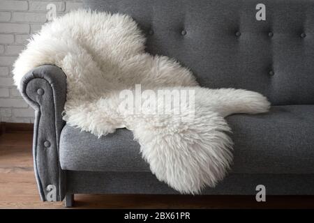 Weiße Schafhaut auf einem grauen Sofa. Ein gemütlicher Ort zum Entspannen in der Wohnung. Moderne Einrichtung im skandinavischen Stil Stockfoto