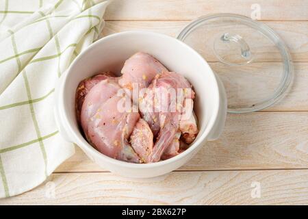 Stücke von frischem rohem Kaninchenfleisch mariniert mit Olivenöl und Knoblauch vor dem Einkochen in einer weißen Keramikpfanne auf dem Küchentisch. Kochen Kaninchen Eintopf. Stockfoto