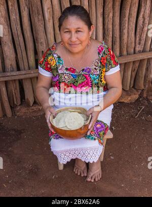 Valladolid, Yucatan/Mexiko - Februar 26,2020: Maya-Frau in ihrem traditionellen Huipilkleid, die eine Schale hält und ihre handgemachten Tortillas vor sich hält Stockfoto