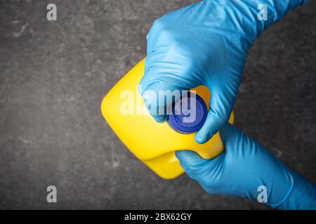 Menschliche Hand im Schutzhandschuh, die eine gelbe Bleichflasche öffnet. Desinfektionskonzept Stockfoto