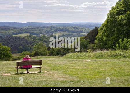 Eine Frau mittleren Alters, die auf einer Bank sitzt und an einem Sommertag die Aussicht von Newlands Corner in den Surrey Hills bewundert, Guildford Surrey England Stockfoto