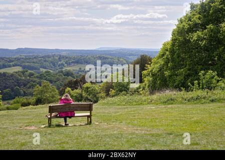 Eine Frau mittleren Alters, die auf einer Bank sitzt und an einem Sommertag die Aussicht von Newlands Corner in den Surrey Hills bewundert, Guildford Surrey England Stockfoto