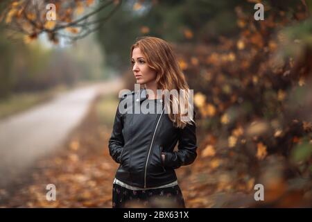 Fabelhafte Rothaarige verträumte Frau mit langen lockigen Haaren auf verschwommenem Herbst Hintergrund. Mädchen auf fabelhaften Hintergrund des Parks mit orangefarbenen Herbstblättern und Roa Stockfoto