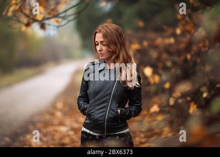 Fabelhafte Rothaarige verträumte Frau mit langen lockigen Haaren auf verschwommenem Herbst Hintergrund. Mädchen auf fabelhaften Hintergrund des Parks mit orangefarbenen Herbstblättern und Roa Stockfoto