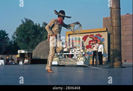 Ein Mann, der Tricks auf der Bühne mit einem Lasso begleitet von einer Blaskapelle, USA in den 1950er Jahren. ‘dträgt traditionelle mexikanische Cowboy (Gaucho) Kleidung, während er in und aus dem Seil tanzt. Er kommt aus der Chicano-Gemeinschaft in den USA – Männer und Frauen mexikanischer Abstammung. Stockfoto