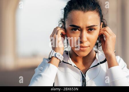 Nahaufnahme Porträt einer schweißtreibendem Sportlerin, die ihre Kopfhörer während eines Trainings justiert Stockfoto