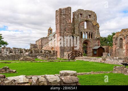 Das imposante befestigte Westtor der dunkelroten Sandsteinkirche des Lundisfarne Priory mit einem noch stehenden Turm und Armbrust-Schleifen sichtbar Stockfoto