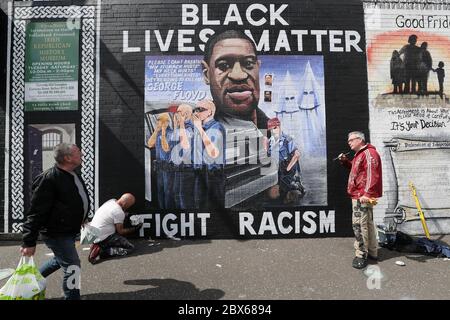 BEACHTEN SIE GRAFISCHE INHALTE AUF WANDMALEREI die Künstler Lyonsie (zweite links) und Micky Doc setzen den letzten Schliff zu einem Wandgemälde von George Floyd an der Belfaster International Wall an der Falls Road. Herr Floyd wurde am 25. Mai in Polizeigewahrsam in der US-Stadt Minneapolis getötet. Das Wandgemälde wurde von Feile an Phobail und Failte Feirste Thiar in Auftrag gegeben und von Marty Lyons und Micky Doherty gemalt. Stockfoto