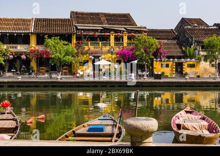 Szene aus der historischen Altstadt von Hoi an am Fluss entlang mit Booten, Laternen, Blumen und den goldgelben Hoi an Gebäuden mit Ziegeldächern Stockfoto