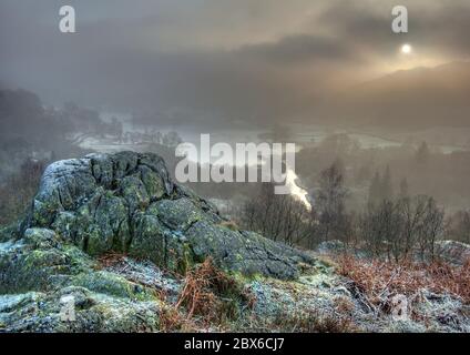 Ein atmosphärischer, frostiger Wintermorgen, mit Sonne gefiltert durch Nebel, mit Blick auf Rydal Wasser von White Moss Common, Lake District, Cumbria, England Stockfoto