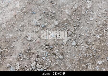 Raue kiesige und steinige Schotterbahn, die in der Sommersonne trocken gebacken wird. Fall auf steinigen Boden Metapher, holprige Fahrt, unebene Oberfläche, raue Textur, raue Straße. Stockfoto