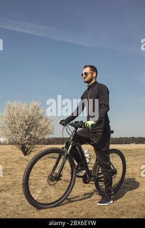 Junger Mann, der mit einem Fuß auf dem Fahrradpedal steht Stockfoto