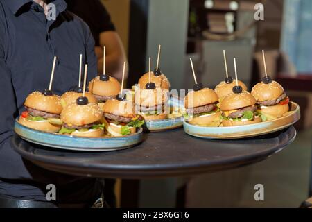 Kellner mit einem Tablett mit Vorspeisen. Outdoor-Party mit Finger Food, Burger, Schieberegler. Mann halten Tablett mit Burger im Restaurant. Männerhände halten ein Stockfoto