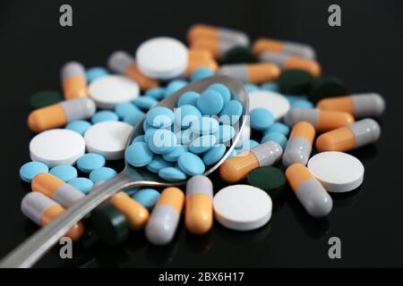 Pillen und Kapseln, Löffel mit verschiedenen Medikamenten und Tabletten auf einem dunklen Glastisch verstreut. Konzept der Apotheke, Antibiotika, Vitamine Stockfoto