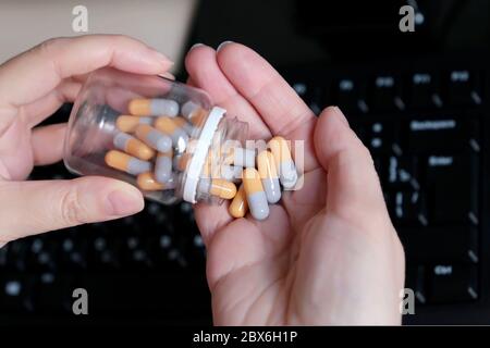 Flasche Pillen in weiblichen Händen auf PC-Tastatur Hintergrund. Frau mit Medikamenten in Kapseln, Konzept der Überarbeit und Stress im Büro Stockfoto