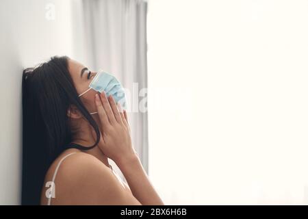 Depressive junge Frau mit Schutzmaske zu Hause Stockfoto