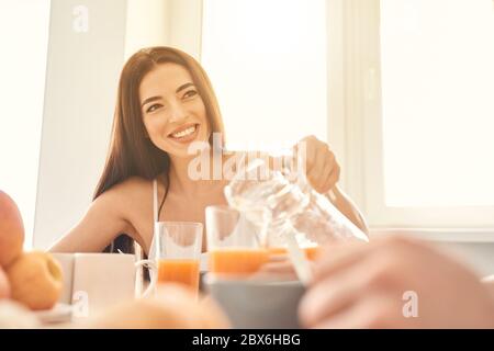 Junge Frau, die Saft in Glas für ihren Mann gießt Stockfoto