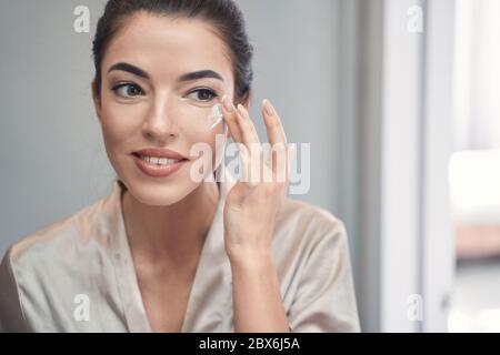 Schöne junge Brünette Anwendung Tagescreme auf ihr Gesicht Stockfoto