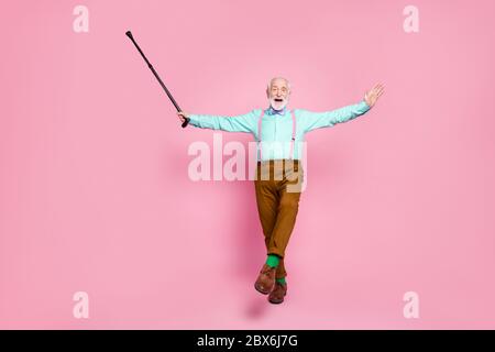 Ganzkörper Foto von aktiven Opa bewegen Tanz Senior Party heben gehen Stick Bein tragen Mint Hemd Hosenträger Fliege Hose Schuhe grüne Socken Stockfoto