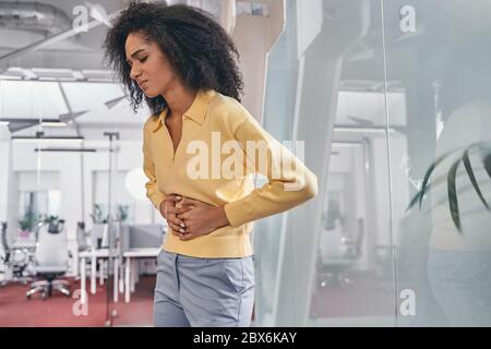 Traurige Frau, die an Magenkrämpfen bei der Arbeit leidet Stockfoto