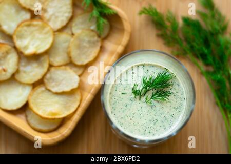 Dill und Sauerrahm Dip für hausgemachte Kartoffelchips vegan: Gesunder Snack mit Dill, Tahini, Wasser, Essig und Zitronensaft im Glas. Dünne Scheiben Stockfoto