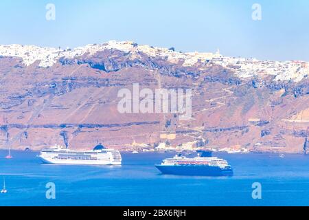 Griechenland. Sonniger Sommertag vor der felsigen Küste von Santorini. Zwei große Kreuzfahrtschiffe und mehrere kleine Segelboote Stockfoto