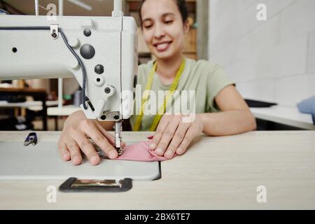 Hände von glücklichen jungen Schneider von elektrischen Nähmaschine arbeiten über Schulterpolster für neues Kleid, Mantel oder andere Kleidungsstück Stockfoto