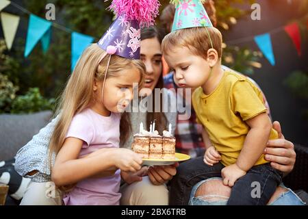 Happy Kids mit Geburtstagshüten, die Kerzen auf den Kuchen blasen Stockfoto