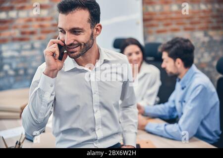 Lächelnder Geschäftsmann, der im Büro mit dem Smartphone spricht Stockfoto