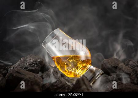 Ein Glas Scotch auf den Felsen, auf einem Bett aus rauchigen Kohle sitzend Stockfoto