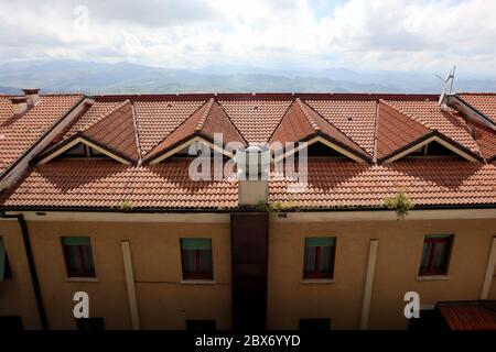 Draufsicht auf Wohngebäude in San Marino, Italien, rote Dachziegel und gelbe Hauswand, Dach mit dreieckigen Oberlichtern an sonnigen Tagen Stockfoto