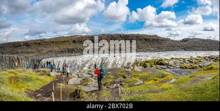 Panoramablick über den größten und mächtigsten Wasserfall Europas, den Dettifoss in Island, in der Nähe des Sees Myvatn, mit dramatischem Himmel und Touristen Stockfoto